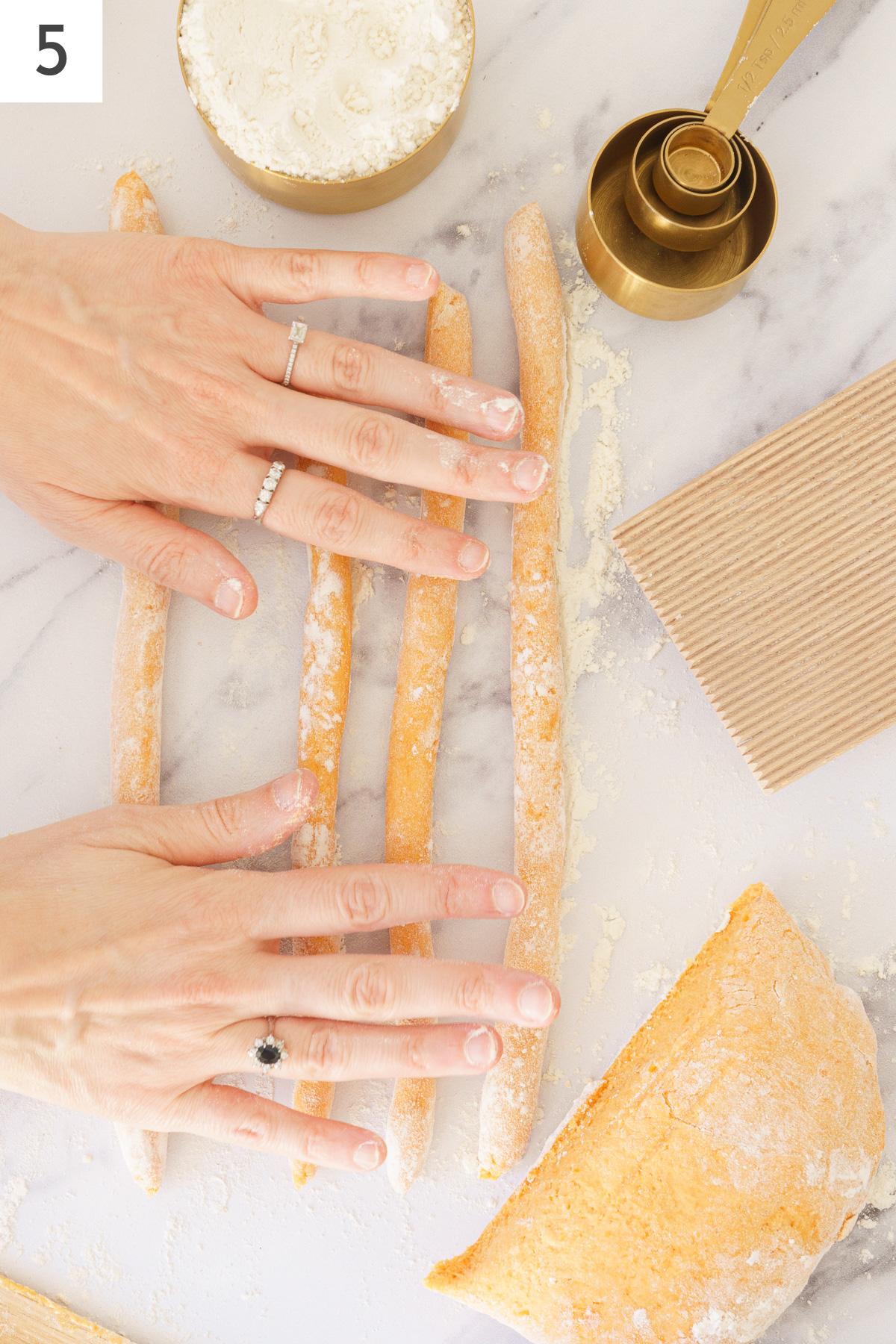 A hands rolling out a small portion of long rope dough.