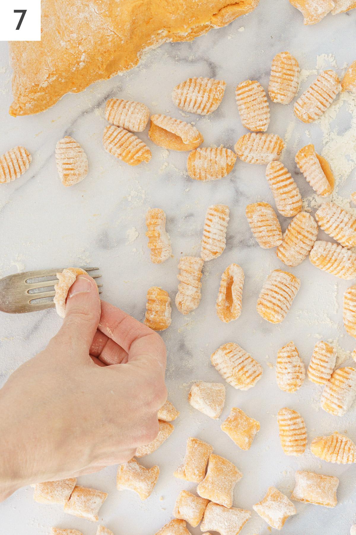 Flour coated pieces of gnocchi dough and making ridges using a fork.