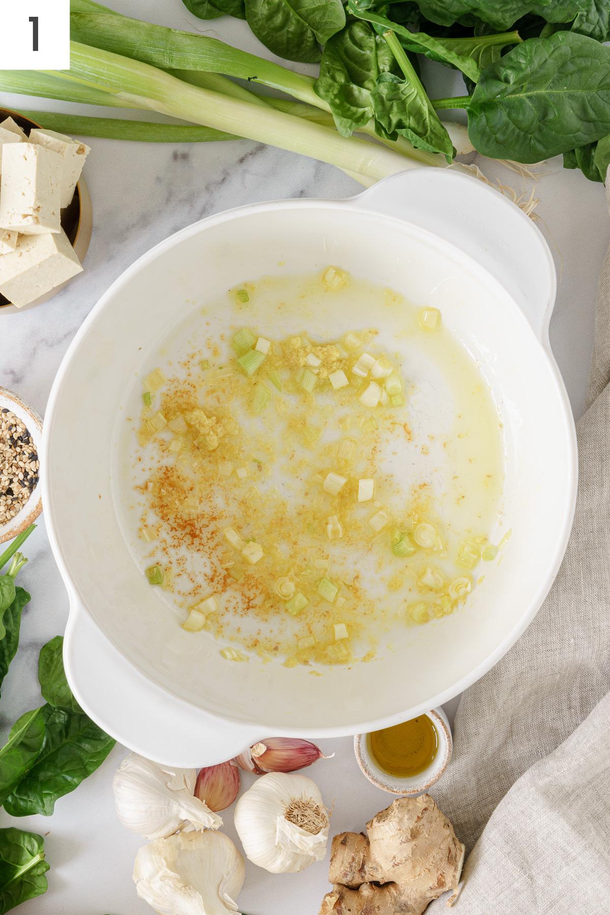 Sauteed green onions, ginger, and minced garlic in a cooking pot.