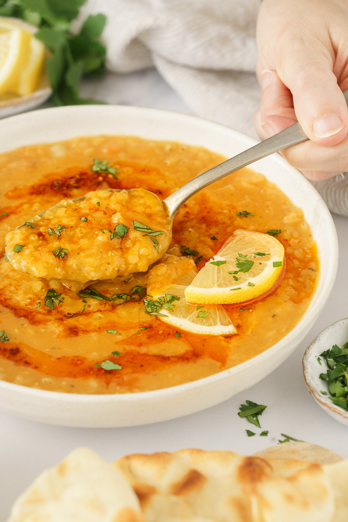 A hand scopping a spoonful of turkish lentil soup with lemon wedges on the side.
