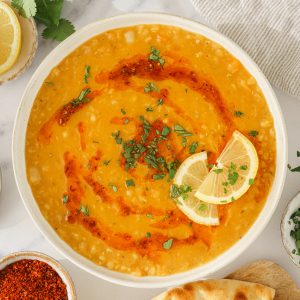 A bowl of turkish lentil soup sprinkled with chopped mint and emon wedges on the side.