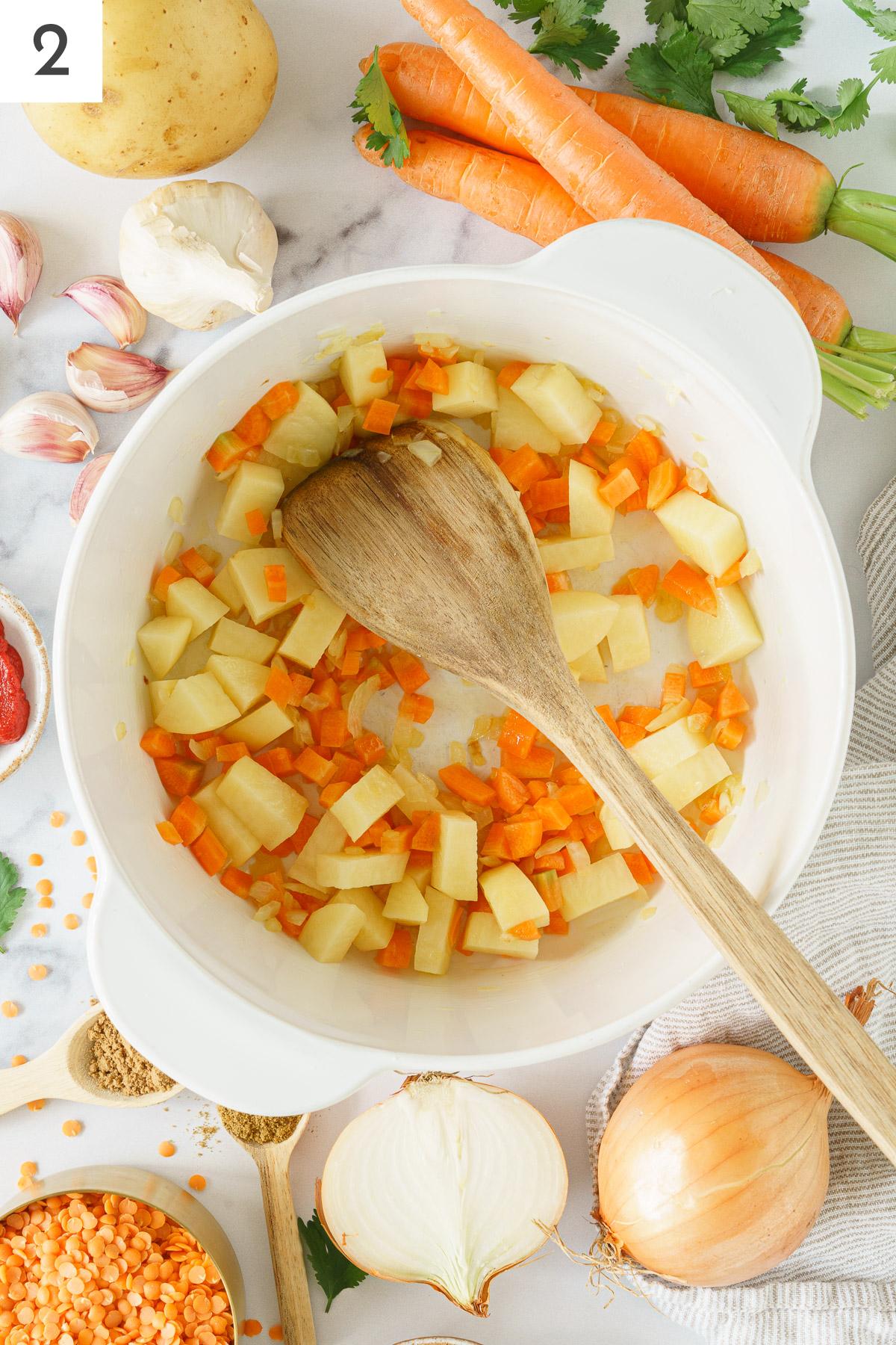 A pot with sauteed onion, cube carrots and potatoes.