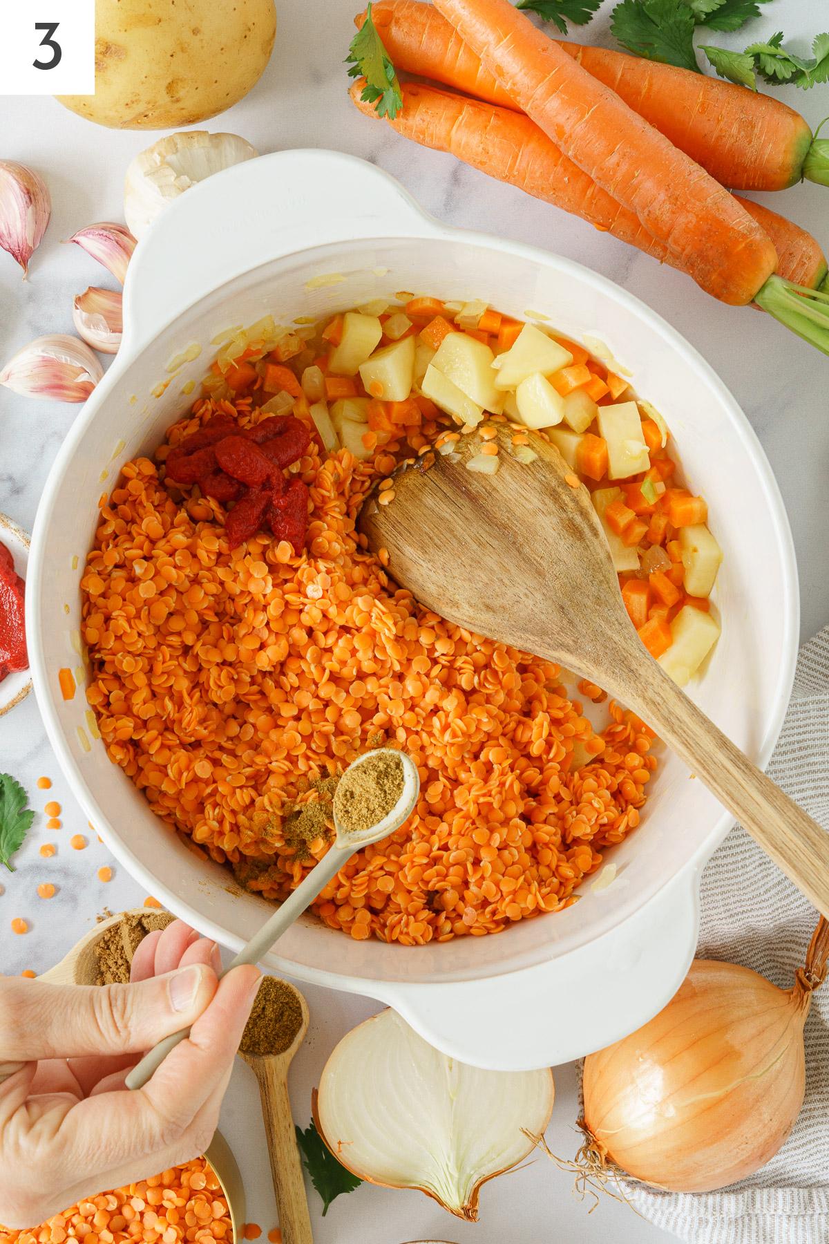 A pot with sauteed carrots, potatoes, red lentils added with cumin powder.