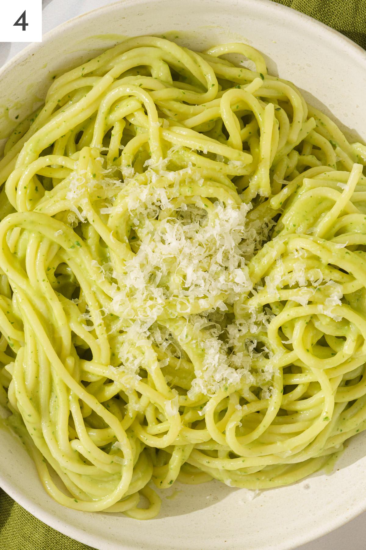 A plate of pasta with avocado sauce topped with grated parmesan cheese.