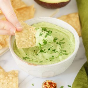 A hand scooping avocado sauce with a taco.