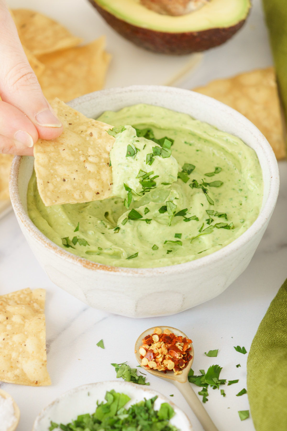 A hand scooping avocado sauce with a taco.