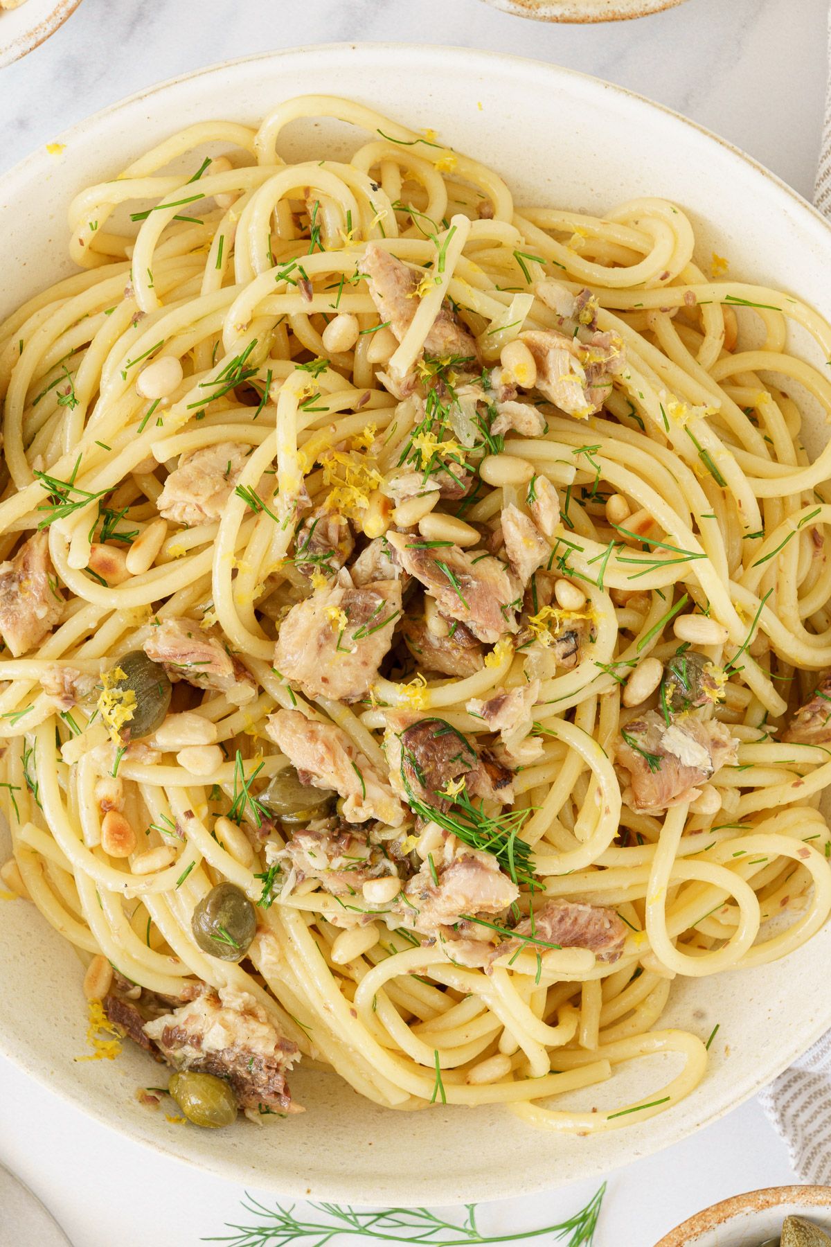 A close up of a plate of mediterranean sardine pasta topped with sardines, pine nuts, and chopped dill.