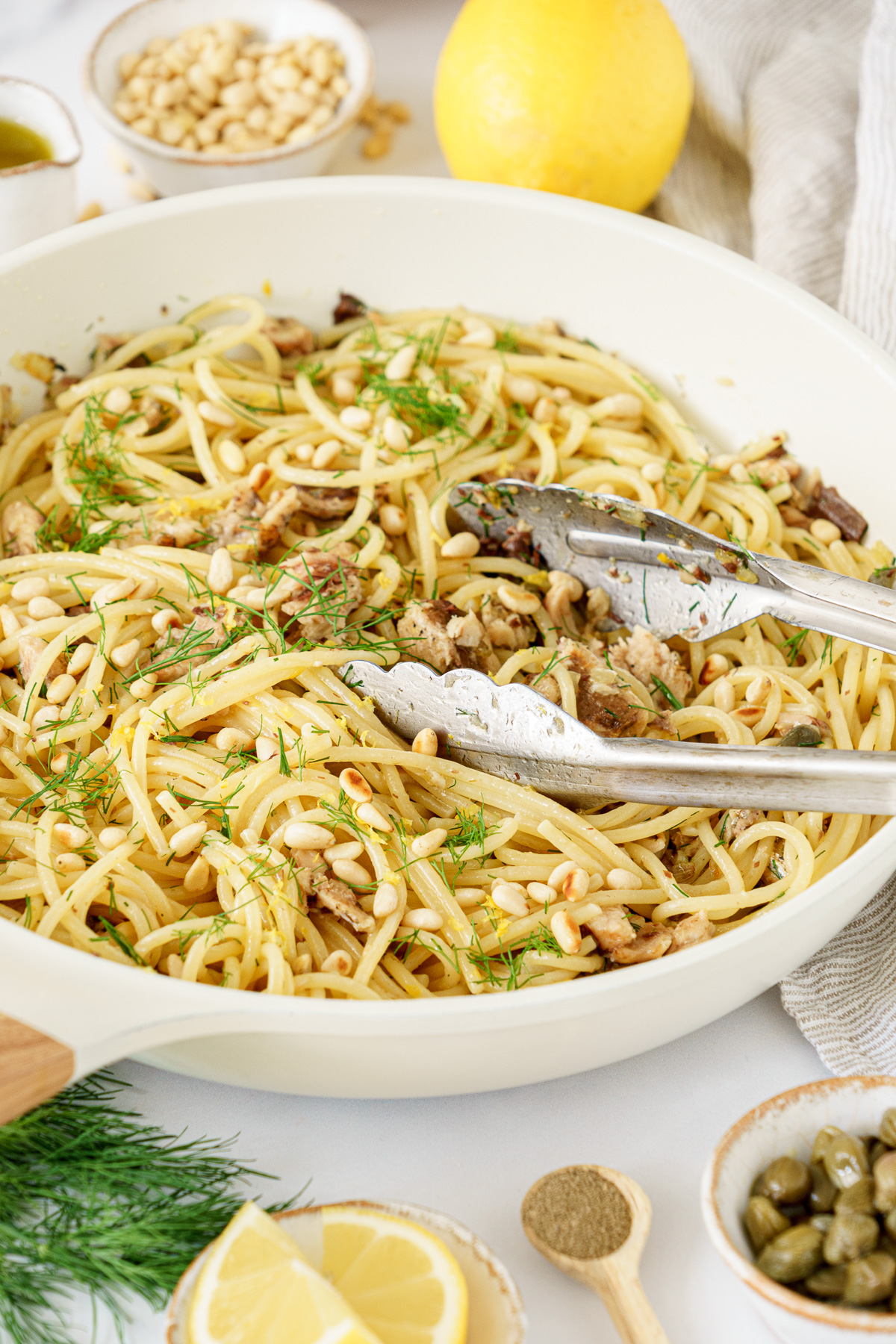 Mediterranean sardine pasta in a pan topped with pine nuts and sardines, garnished with chopped dill.