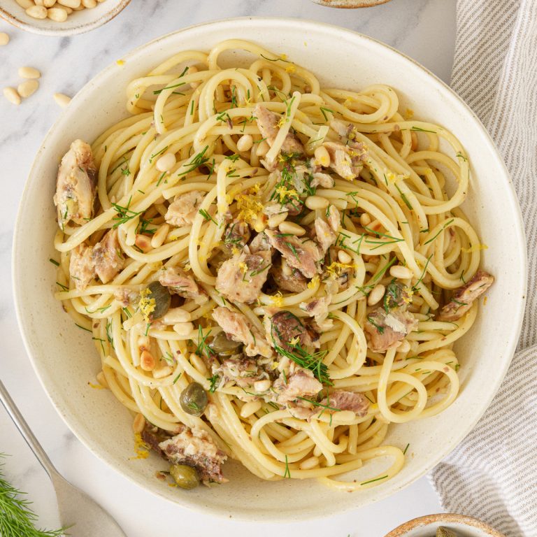 A plate of mediterranean sardinee pasta topped with sardines, pine nuts, and chopped dill.