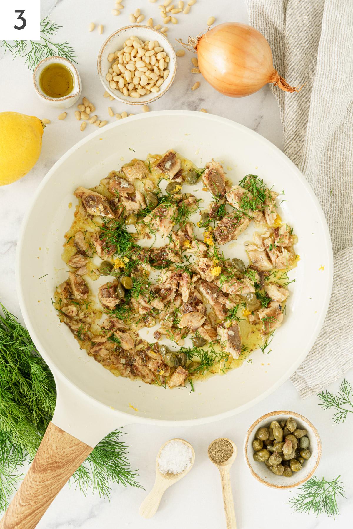 A pan with sauteed onions, sardines, and capers added with dill.