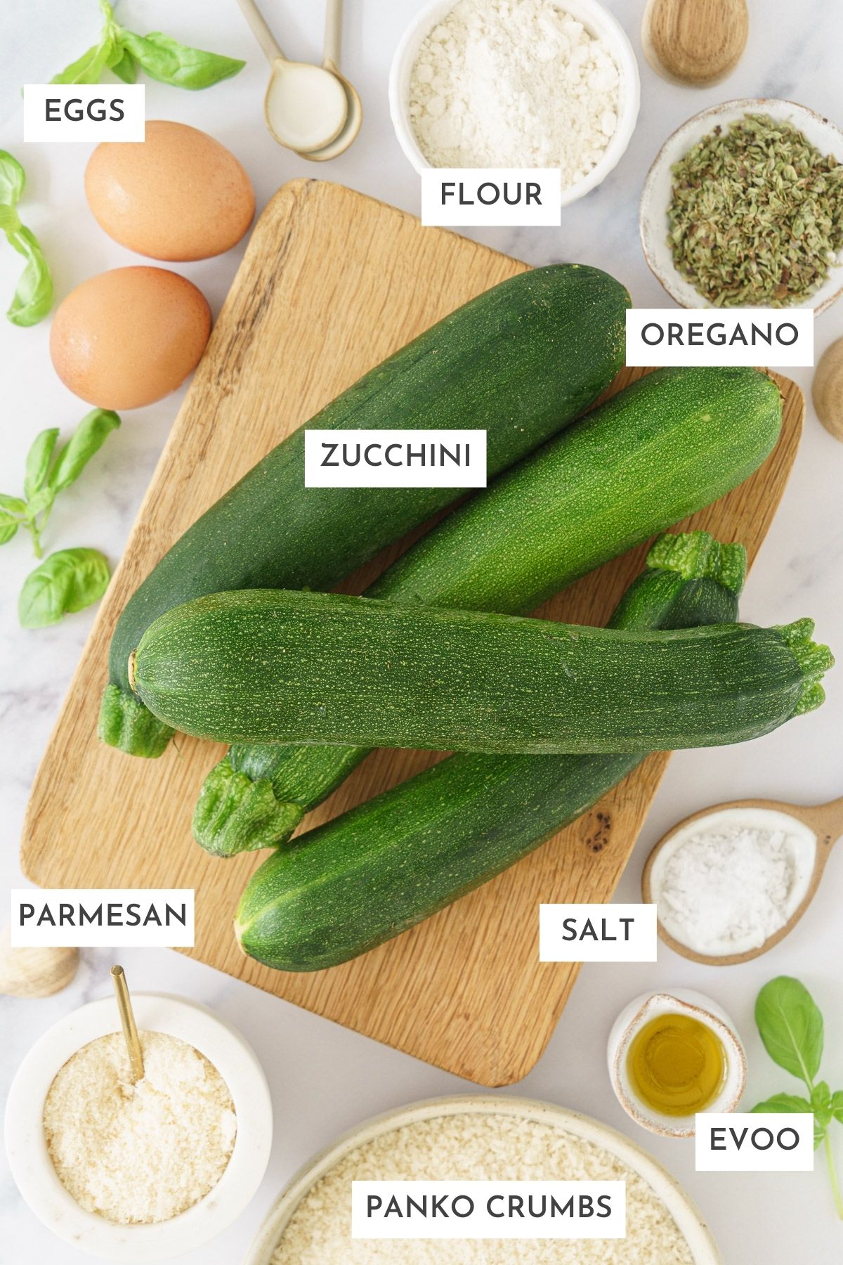 Laid out ingredents of baked zucchini fries: Aggs, flour, oregano, zucchini, parmesan, salt, evoo, and panko crumbs.