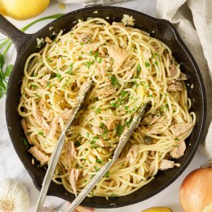 A skillet with all the ingredients for canned tuna pasta, being tossed together with tongs.