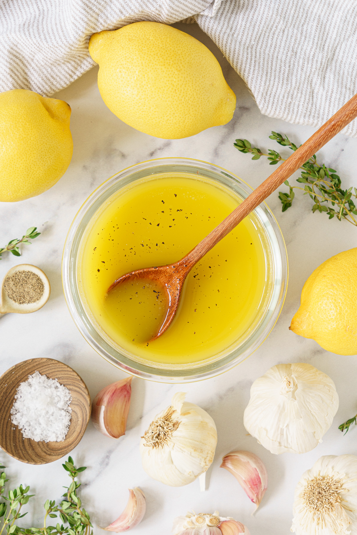 A glass container of lemon vinaigrette and a wooden spoon sprinkled with pepper.