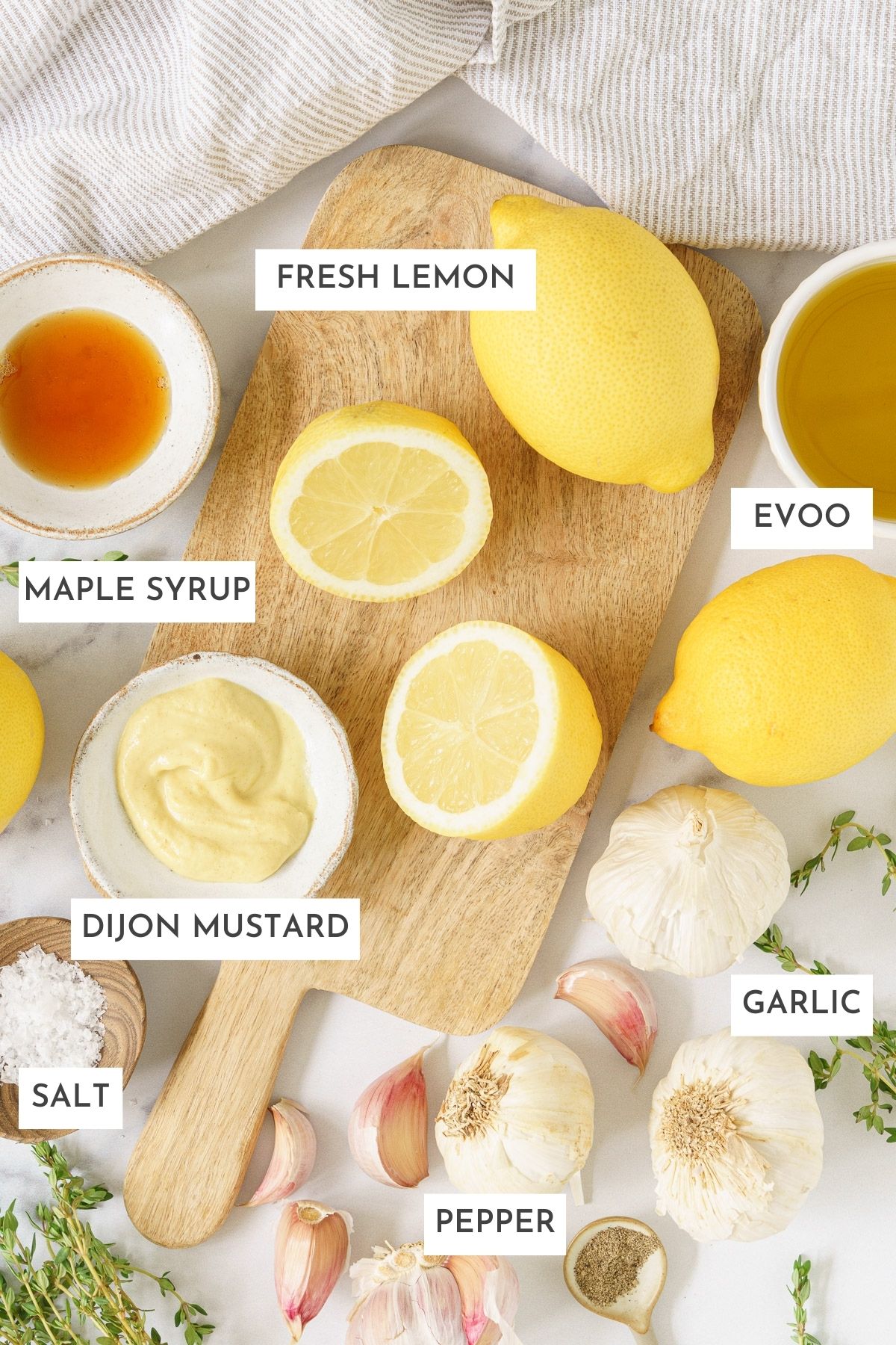 Laid out ingredients of lemon vinaigrette: fresh lemon, evoo, maple syrup, dijon mustard, garlic, salt and pepper.