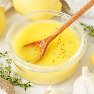 Lemon vinaigrette and a wooden spoon in a glass container sprinkled with pepper.