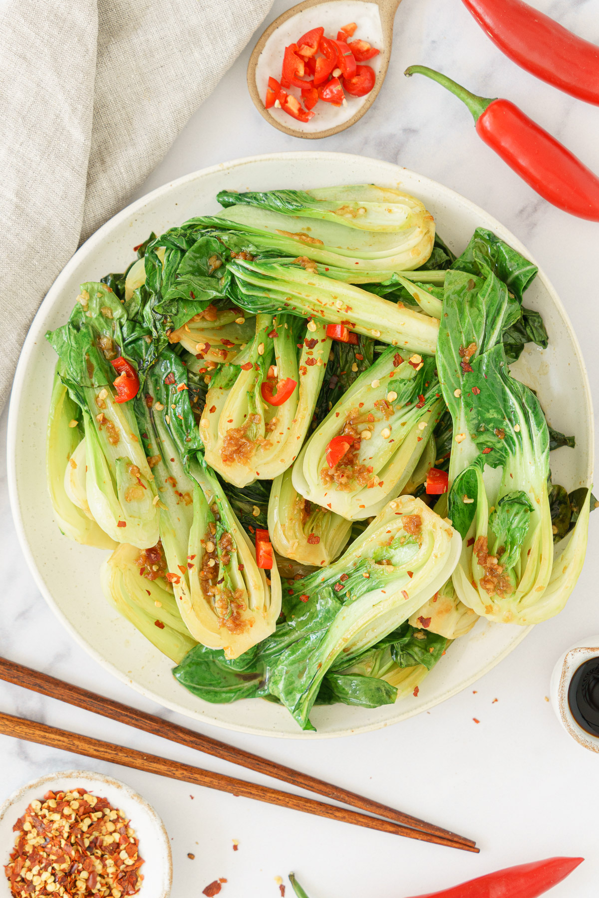 A round dish filled with bok choy, topped with chili flakes and sautéed chopped garlic.