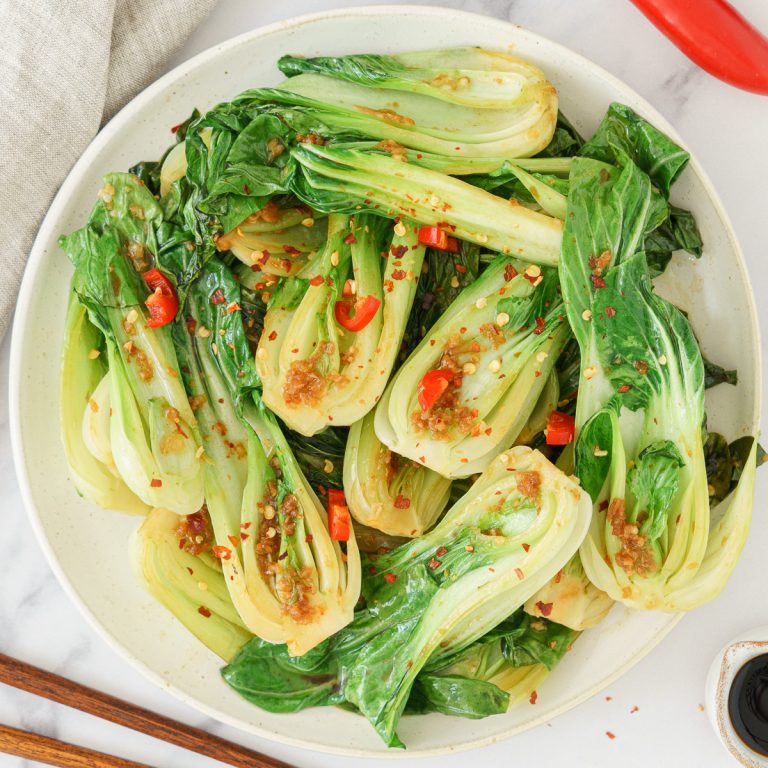 A plate of bok choy sprinkled with chili flakes and garlic, arranged on a round dish.