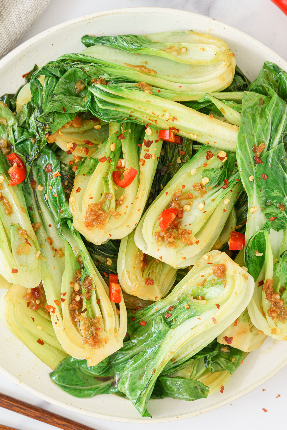 A plate of bok choy sprinkled with chili flakes and garlic, arranged on a round dish.