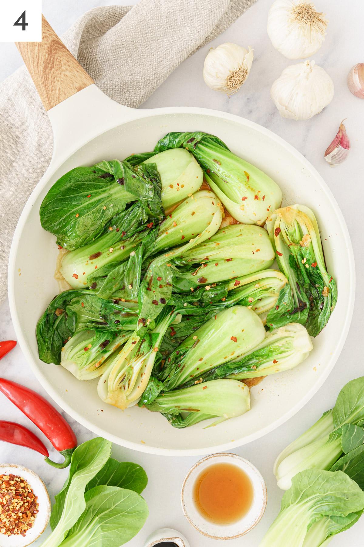 Bok choy and sautéed chopped garlic mixed together in a skillet.